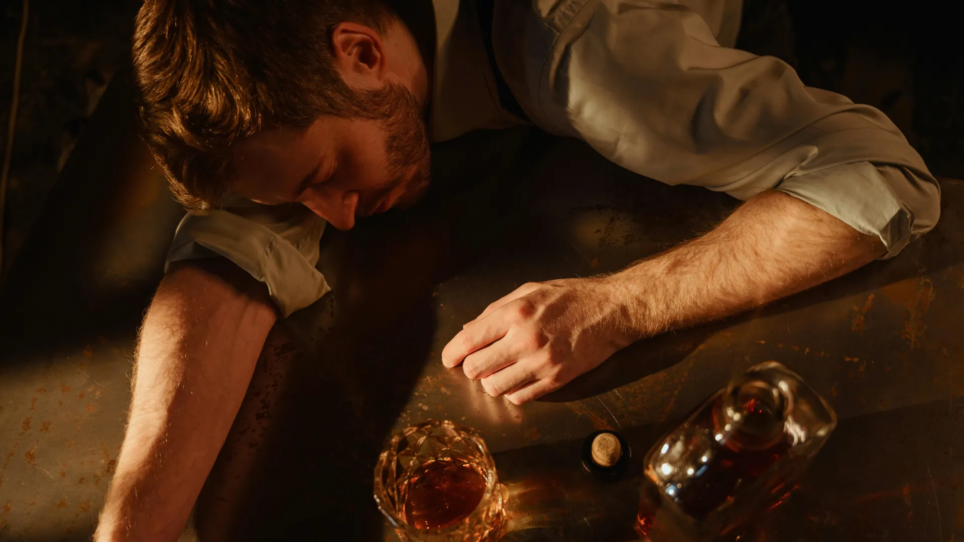A young man is passed out on the floor next to bottle of whiskey. A classic case of alcohol addiction.