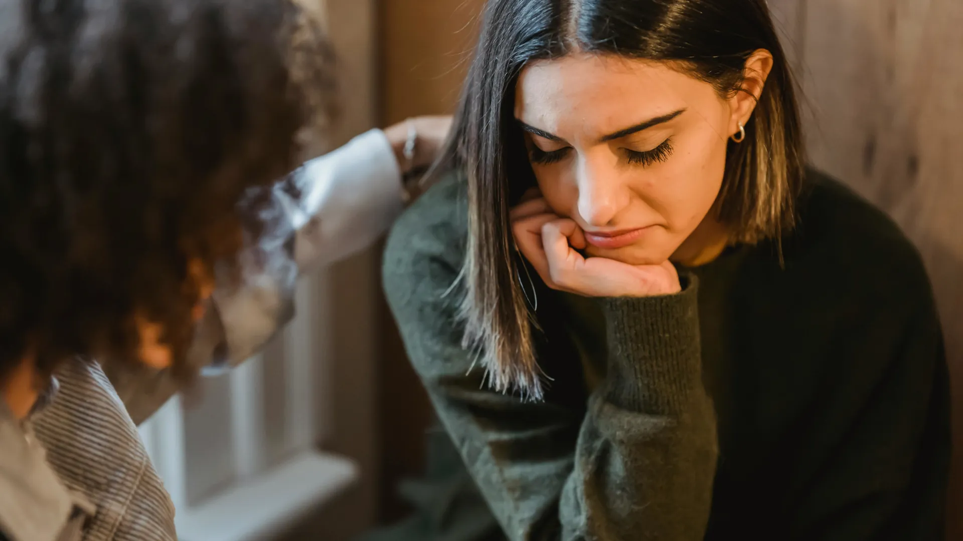 A young woman is comforted by her friend as she looks visibly upset.