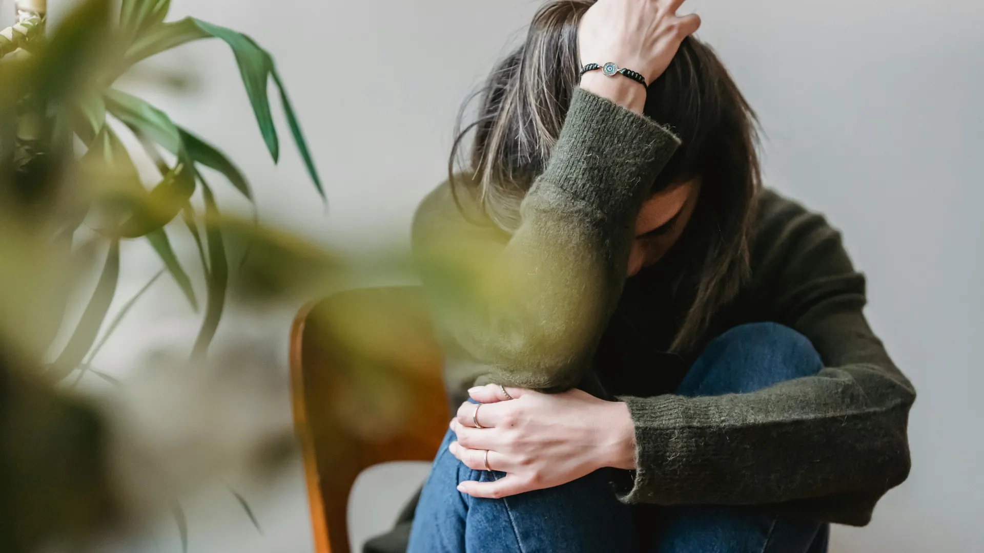 A young woman is cradling herself with her arm over her head, appearing deeply troubled and worried.
