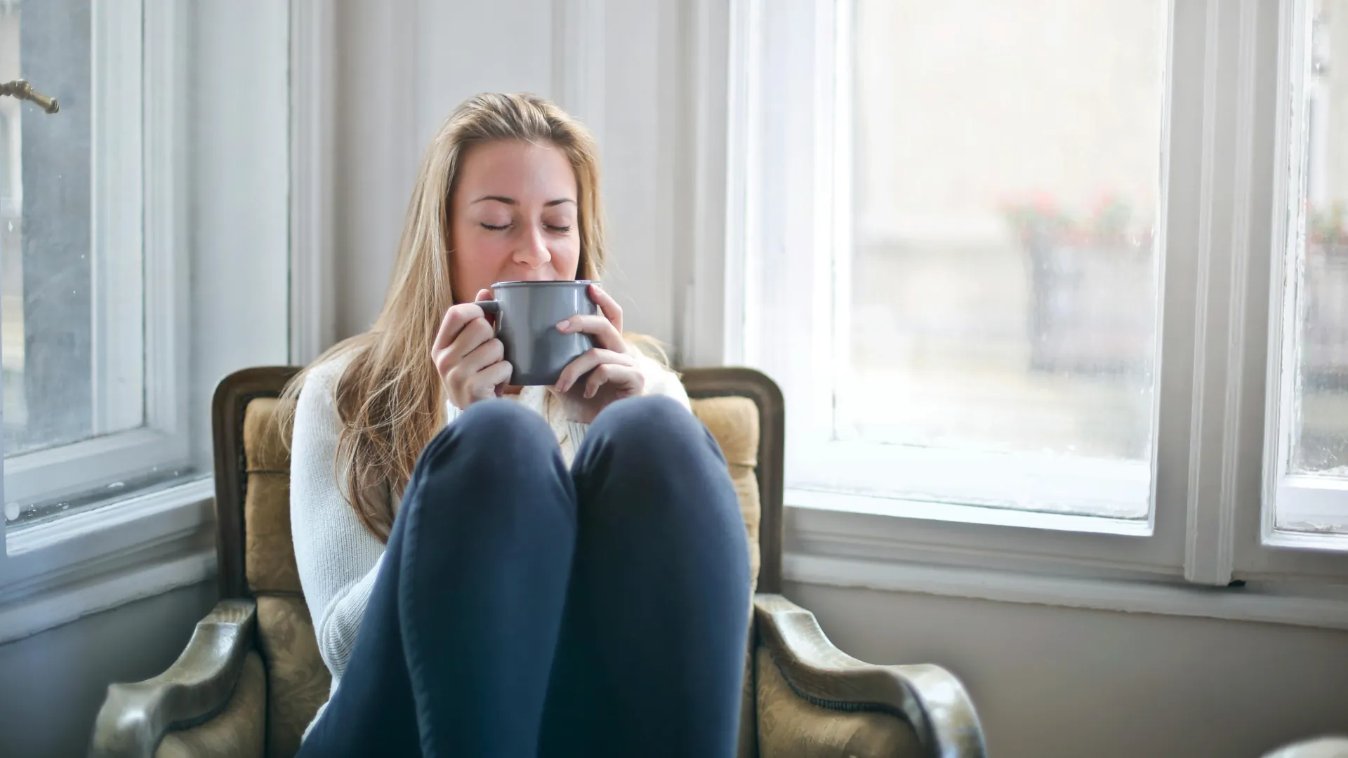A woman is sitting with a cup of tea in a relaxed state on her chair, free of any worries.